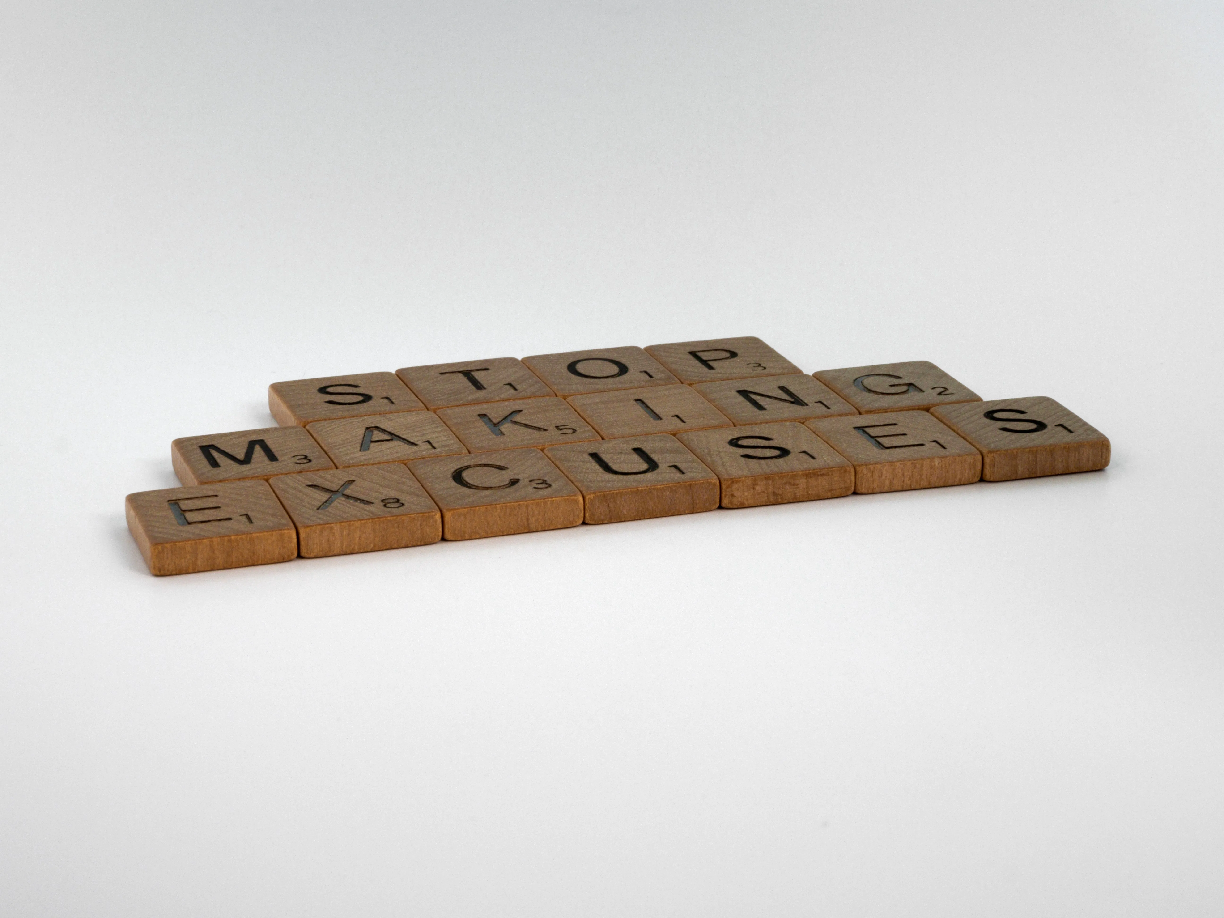 Scrabble board pieces spelling out 'stop making excuses'